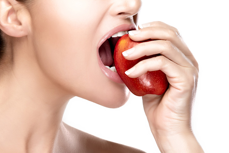 Closeup of beautiful and healthy mouth biting a red apple. Closeup portrait isolated on white background